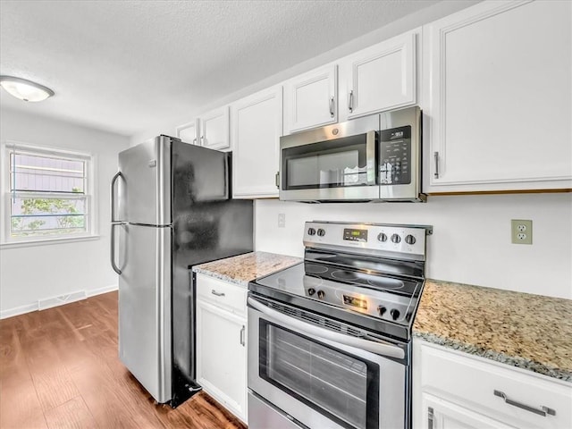 kitchen with light stone countertops, appliances with stainless steel finishes, white cabinetry, wood finished floors, and visible vents