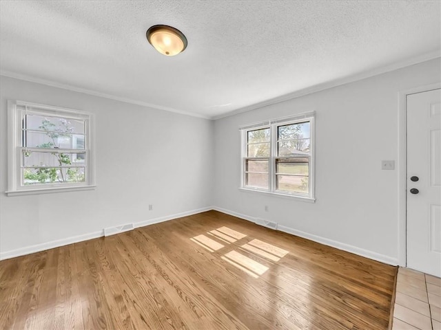 spare room featuring visible vents, ornamental molding, a textured ceiling, and light wood-type flooring