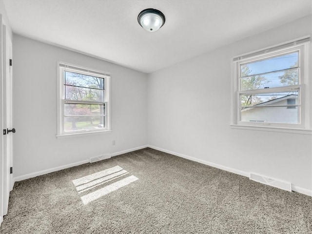 carpeted spare room featuring baseboards, visible vents, and plenty of natural light