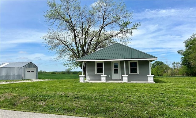 view of front of house featuring a porch, a garage, a front lawn, an outbuilding, and metal roof