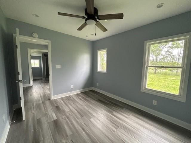 unfurnished room featuring plenty of natural light, a ceiling fan, wood finished floors, and baseboards