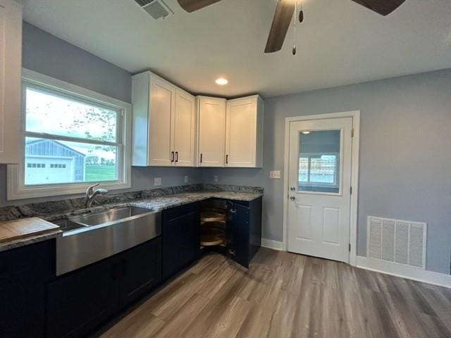 kitchen with a ceiling fan, light wood-type flooring, a sink, white cabinets, and baseboards
