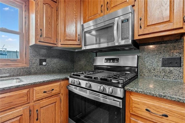 19707 E State Route A, Archie, MO 64725 - kitchen with stainless steel appliances, tasteful backsplash, brown cabinetry, and dark stone countertops