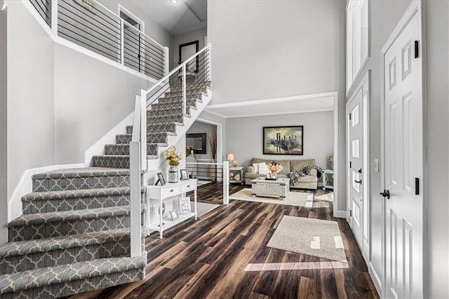 foyer featuring baseboards, dark wood-style flooring, a towering ceiling, and stairway