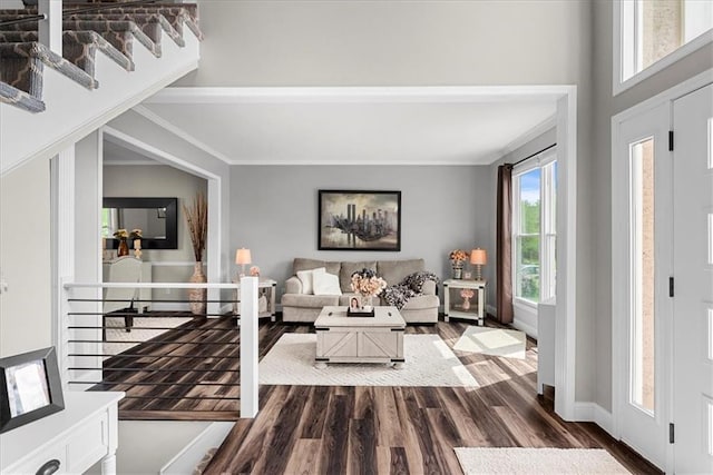 living room featuring crown molding, baseboards, dark wood-style flooring, and stairs