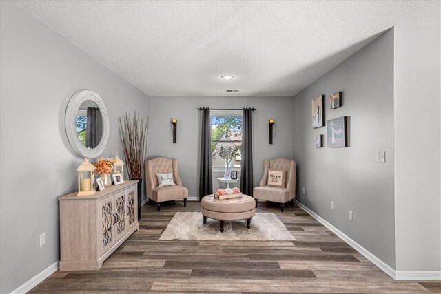 sitting room with baseboards, a textured ceiling, and wood finished floors