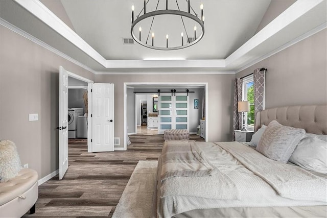 bedroom with visible vents, lofted ceiling, washer and dryer, wood finished floors, and a chandelier