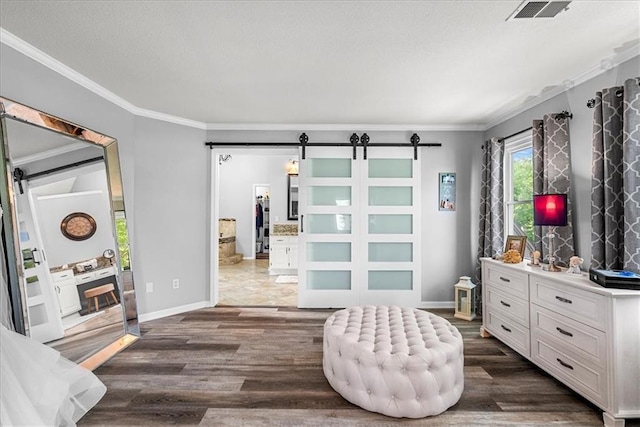 bedroom featuring visible vents, crown molding, dark wood finished floors, a barn door, and baseboards