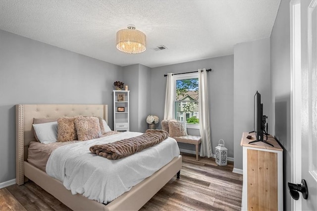 bedroom featuring visible vents, a textured ceiling, baseboards, and wood finished floors