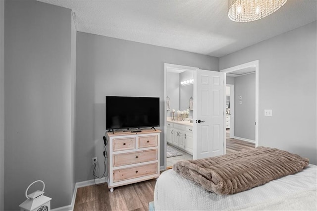 bedroom with baseboards, ensuite bath, wood finished floors, and an inviting chandelier