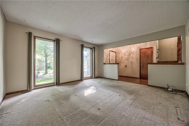 unfurnished living room with carpet flooring, a textured ceiling, and baseboards