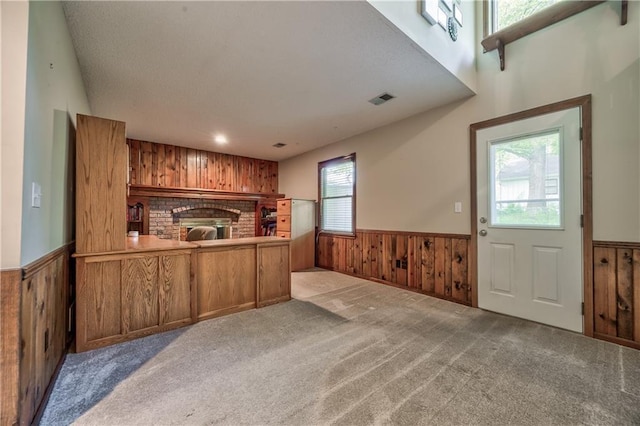 unfurnished living room with wainscoting, wooden walls, carpet, and a fireplace