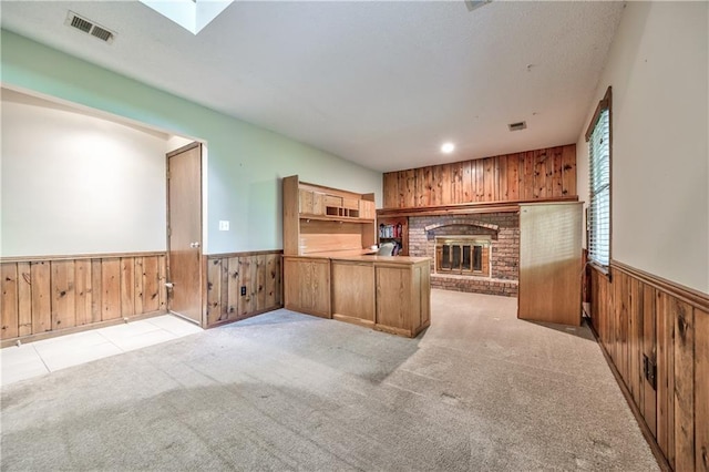 unfurnished living room featuring wooden walls, a wainscoted wall, light carpet, a fireplace, and a skylight