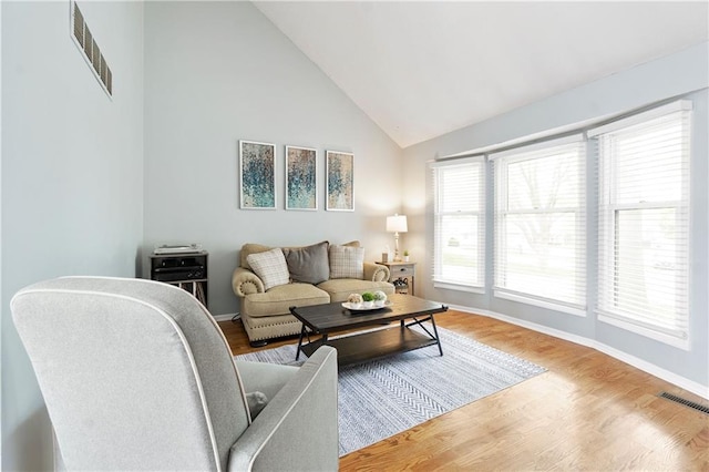 living area with high vaulted ceiling, baseboards, wood finished floors, and visible vents