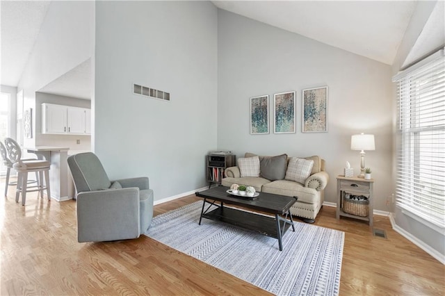 living room featuring visible vents, light wood-style floors, a healthy amount of sunlight, and high vaulted ceiling