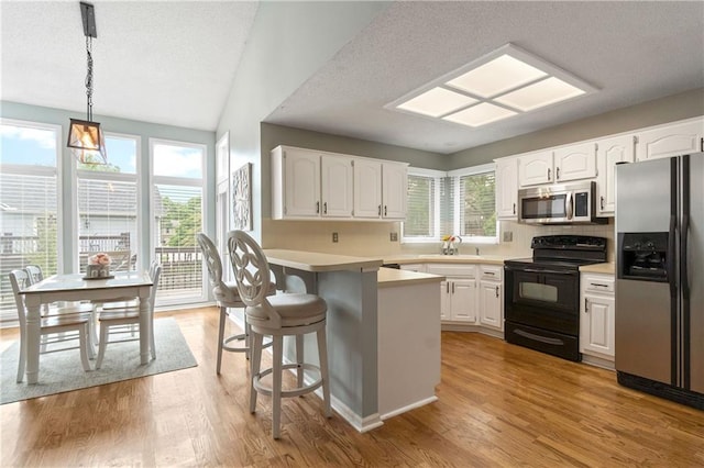 kitchen with appliances with stainless steel finishes, white cabinets, a breakfast bar, and light wood-style flooring