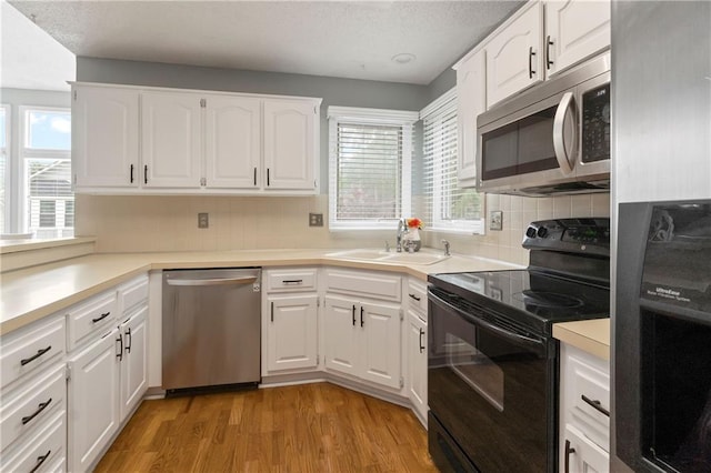 kitchen featuring tasteful backsplash, a sink, light wood-style floors, stainless steel appliances, and white cabinetry