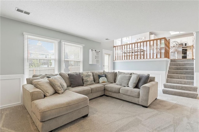 living area featuring carpet flooring, a textured ceiling, a wainscoted wall, visible vents, and stairway