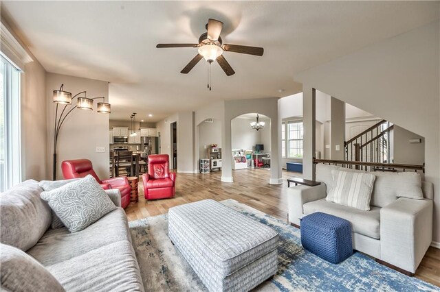 living area with plenty of natural light, ceiling fan with notable chandelier, light wood finished floors, and stairs