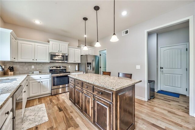 kitchen featuring visible vents, light wood-style flooring, tasteful backsplash, and stainless steel appliances