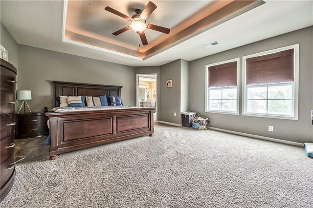 carpeted bedroom with a ceiling fan, a tray ceiling, visible vents, and baseboards