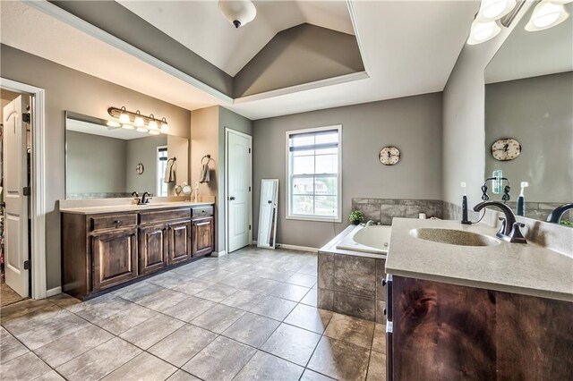 bathroom with a garden tub, tile patterned flooring, vaulted ceiling, vanity, and a raised ceiling