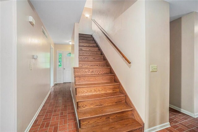 stairs with visible vents, baseboards, and brick patterned floor