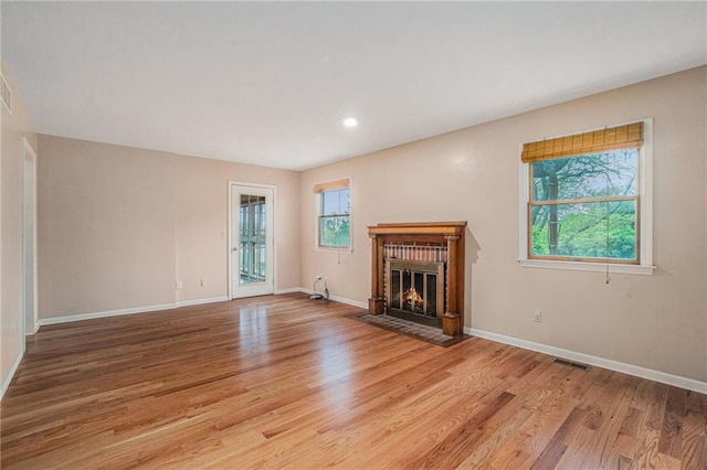 unfurnished living room featuring visible vents, a fireplace with flush hearth, light wood-style floors, and baseboards