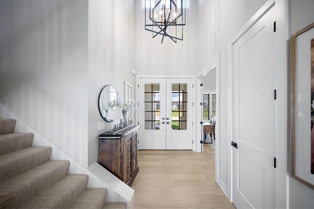 entryway with french doors, a towering ceiling, light wood finished floors, a chandelier, and stairs