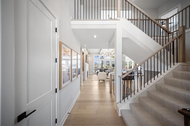 stairway featuring a towering ceiling, wood finished floors, baseboards, recessed lighting, and a chandelier
