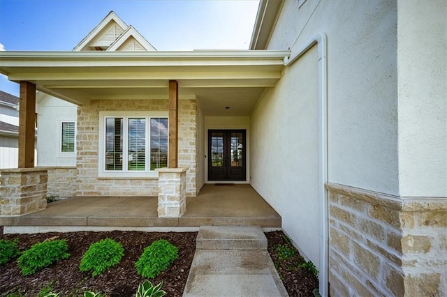 property entrance with stucco siding, french doors, stone siding, and covered porch