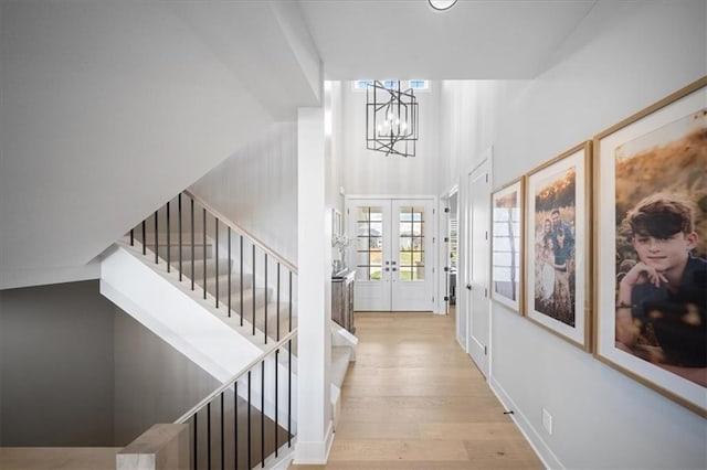 entrance foyer featuring french doors, wood finished floors, an inviting chandelier, a high ceiling, and stairs