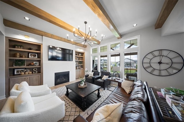 living room featuring an inviting chandelier, built in shelves, beam ceiling, and a glass covered fireplace