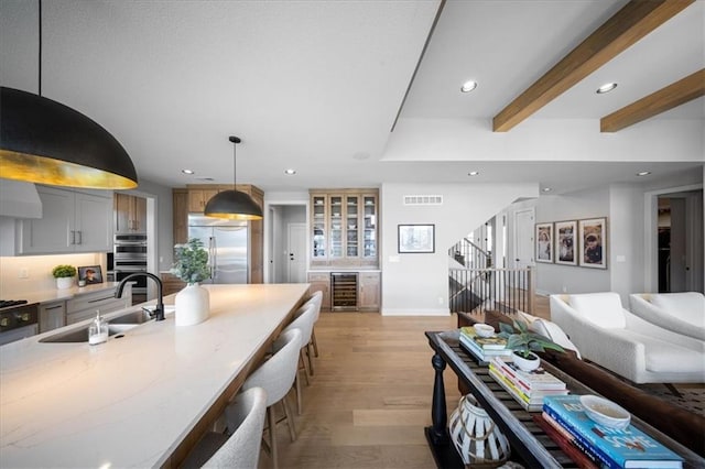 kitchen with appliances with stainless steel finishes, a sink, beverage cooler, recessed lighting, and light wood-style flooring