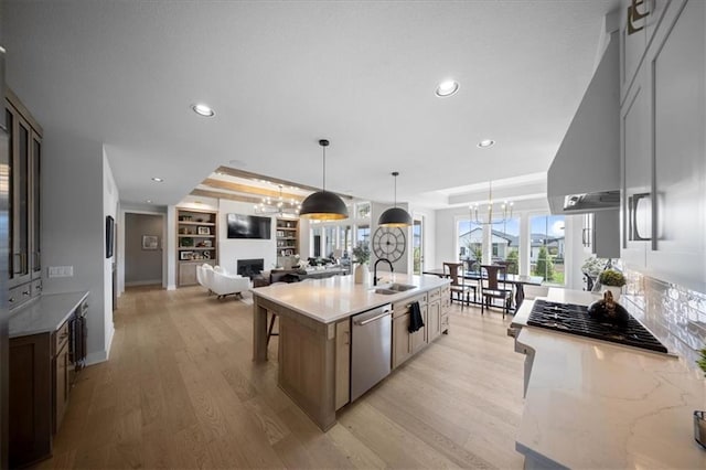 kitchen featuring an inviting chandelier, a large island with sink, light stone counters, light wood-style flooring, and stainless steel appliances