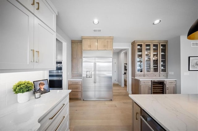 kitchen with appliances with stainless steel finishes, light wood-style floors, beverage cooler, visible vents, and glass insert cabinets