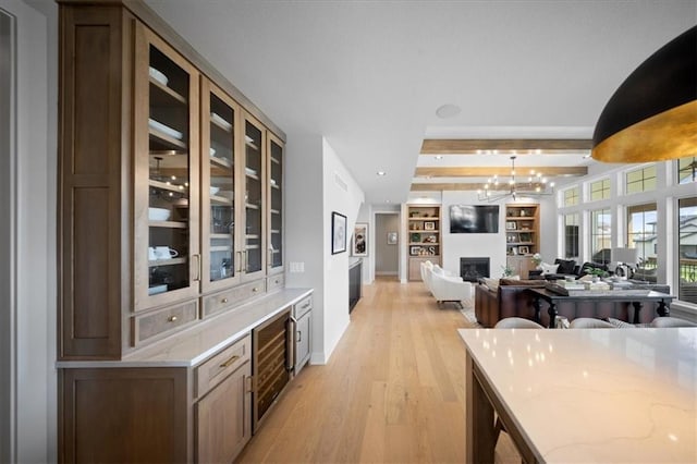kitchen featuring light stone countertops, light wood finished floors, a fireplace, open floor plan, and glass insert cabinets