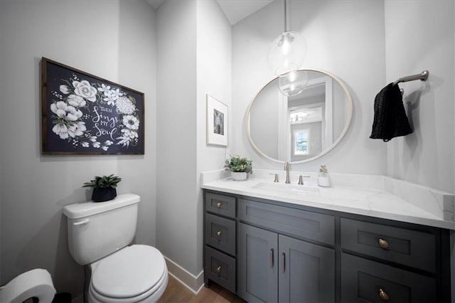 half bath with vanity, baseboards, toilet, and wood finished floors