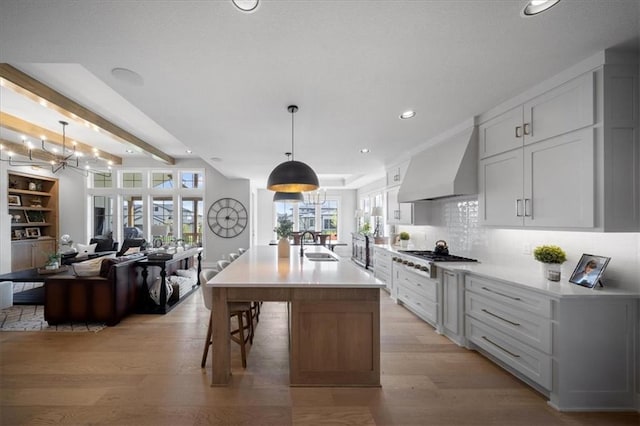 kitchen with light countertops, wall chimney exhaust hood, gas stovetop, a sink, and light wood finished floors