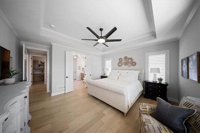 bedroom featuring light wood-style floors, a tray ceiling, and multiple windows