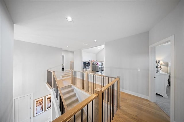 hallway with recessed lighting, wood finished floors, and an upstairs landing