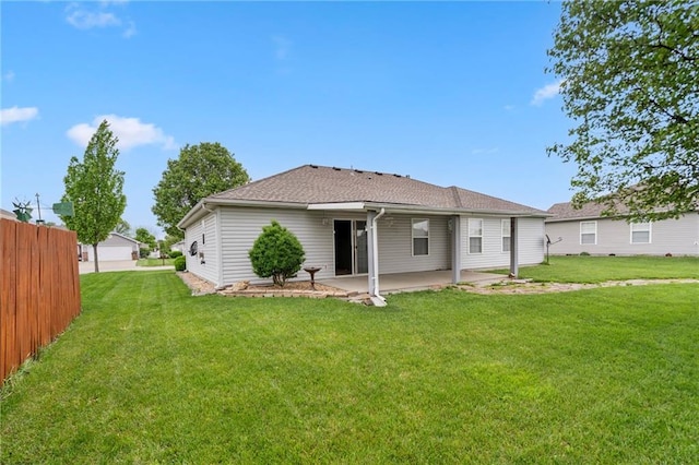 rear view of property with a lawn, fence, a shingled roof, and a patio area