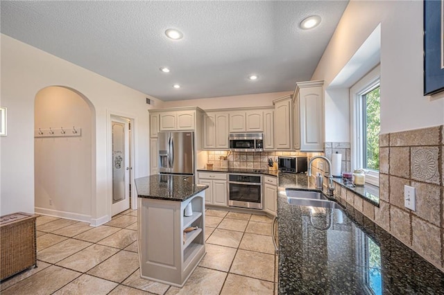 kitchen with open shelves, a sink, arched walkways, dark stone counters, and stainless steel appliances
