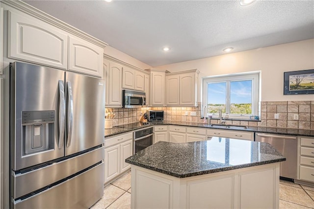 kitchen with backsplash, stainless steel appliances, a sink, and dark stone countertops
