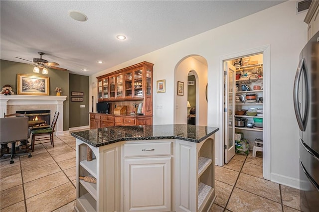 kitchen featuring visible vents, open shelves, a ceiling fan, freestanding refrigerator, and arched walkways