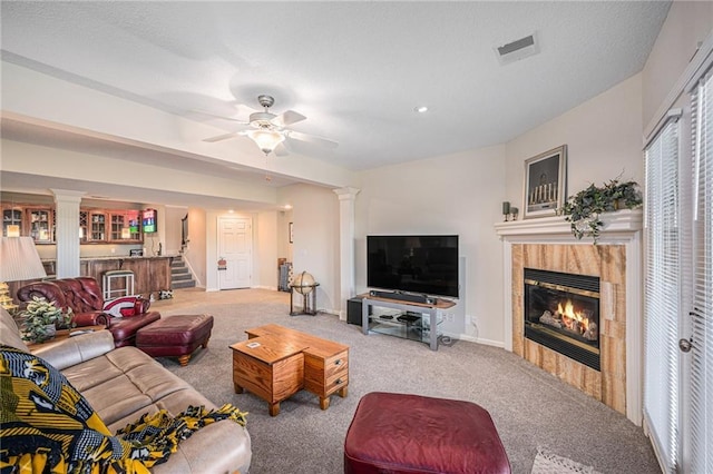 carpeted living room with visible vents, decorative columns, ceiling fan, and a fireplace