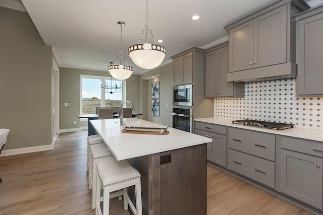 kitchen with a sink, gray cabinets, appliances with stainless steel finishes, and a center island with sink