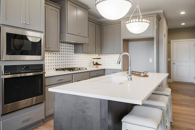 kitchen featuring appliances with stainless steel finishes, gray cabinets, recessed lighting, decorative backsplash, and a center island with sink
