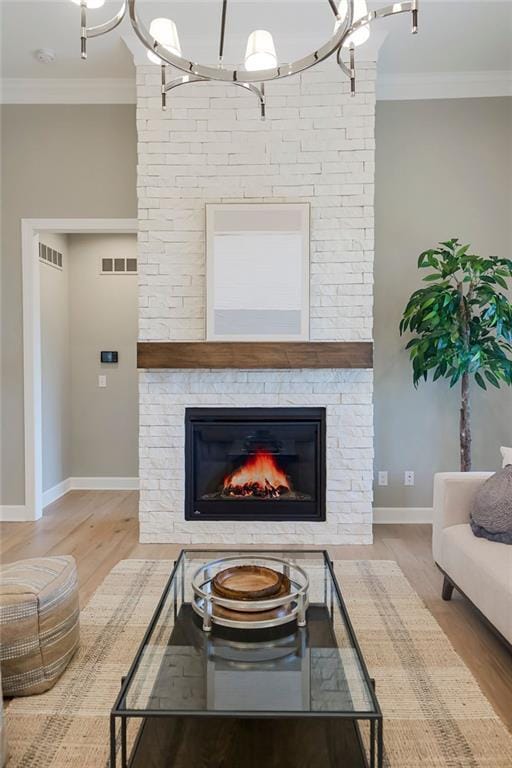 living area featuring visible vents, crown molding, wood finished floors, baseboards, and a stone fireplace