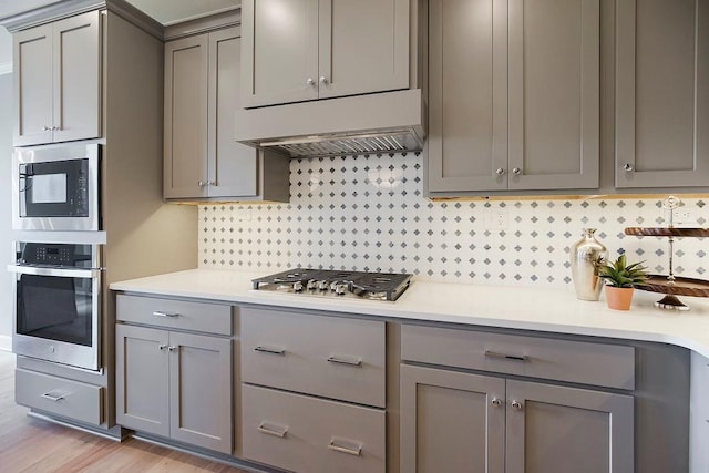 kitchen featuring decorative backsplash, light countertops, ventilation hood, appliances with stainless steel finishes, and gray cabinetry